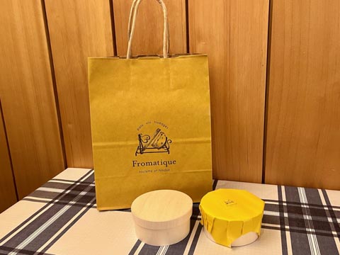 お持ち帰り用の紙袋と包装紙に包まれたチーズケーキ