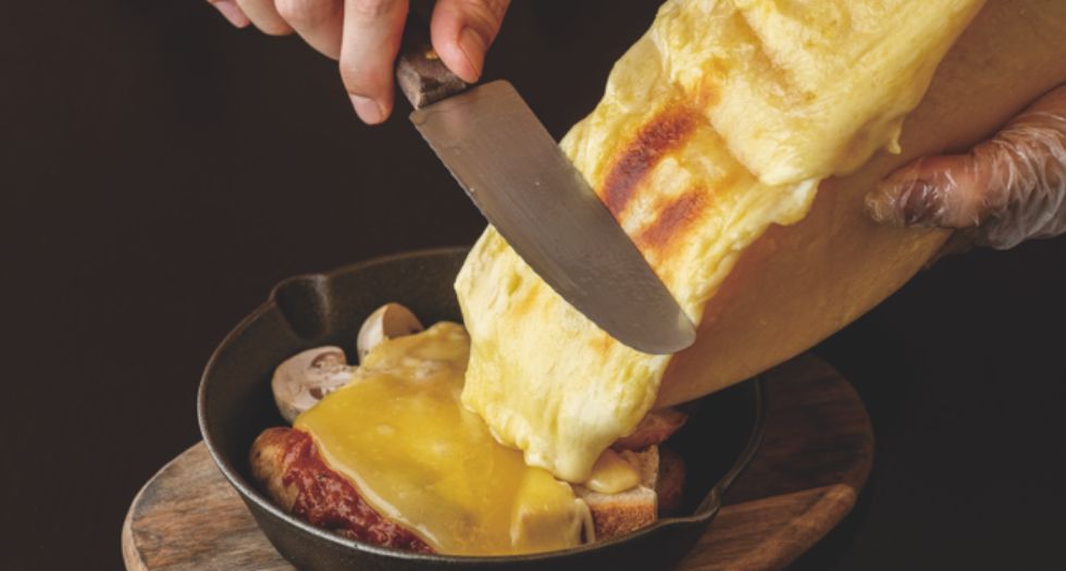 温めたラクレットチーズをプレートの上のジャガイモやソーセージにかける